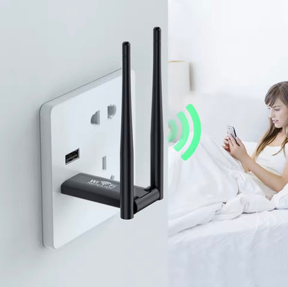 Wireless router with antennas attached to a wall socket, with a person using a smartphone in the background.